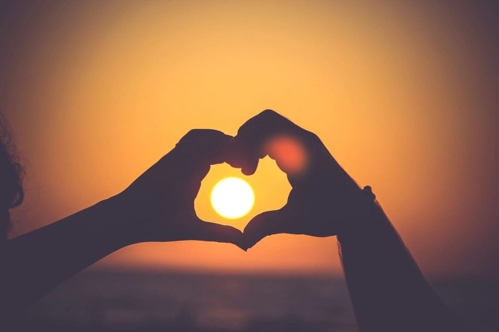 A person making a heart with their hands at sunset.